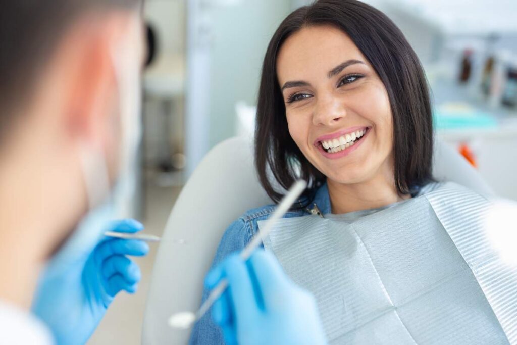 Person brushing teeth beside a bathroom sink with a soft toothbrush, toothpaste, and floss visible.
